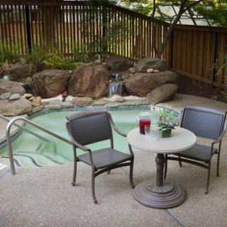 A serene outdoor patio area with a small pool, surrounded by rocks and plants, featuring a table and two chairs.