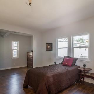 A cozy bedroom with a single bed, wooden floor, and natural light coming through the windows.