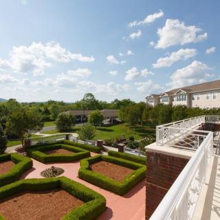 A scenic view from a balcony overlooking a landscaped garden with lush greenery and a partly cloudy sky.