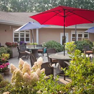 A cozy patio area with tables, chairs, and colorful umbrellas surrounded by lush plants and flowers.
