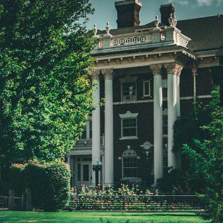 A stately historic mansion featuring elegant columns and surrounded by lush greenery.