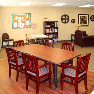 A cozy meeting room with a conference table, surrounded by chairs and decorated with art and bookshelves.