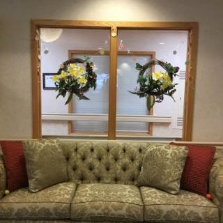 A cozy waiting area featuring a tufted sofa and floral decorations behind glass doors.