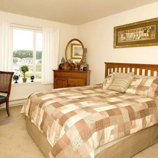 A cozy bedroom with a checkered bedspread, dresser and mirror, and a window offering natural light.