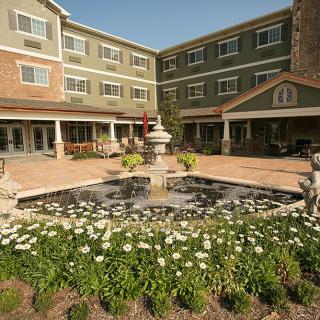 A picturesque courtyard with a central fountain surrounded by flowers in front of a multi-story building.