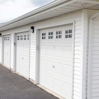 A row of white garage doors along a paved driveway.