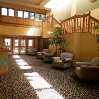 A spacious lobby with armchairs, stairs, and natural sunlight streaming in.