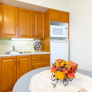 A cozy kitchen with wooden cabinets, a microwave, and a refrigerator featuring autumn-themed decorations on the table.