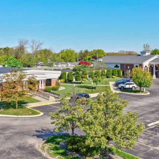 A suburban complex with landscaped grounds and multiple buildings, surrounded by a parking lot on a clear day.