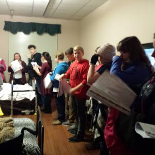 A group of young individuals gathered indoors, engaged in a discussion while holding papers.
