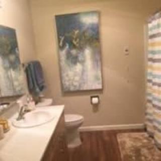 A well-decorated bathroom featuring a large painting, a sink with towels, a toilet, and a colorful shower curtain.