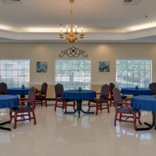 A well-lit dining room with blue tablecloths covering round tables and chairs arranged around them.