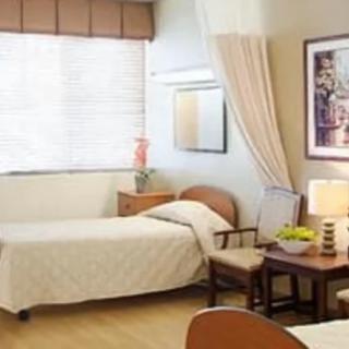 A hospital room with two beds, a table with chairs, and a window with blinds.