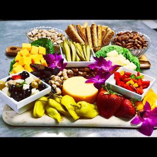 A vibrant cheese and charcuterie board featuring a variety of cheeses, fresh fruits, vegetables, nuts, and crackers elegantly arranged with decorative flowers.