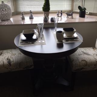 A cozy dining setup with a small round table and bench seating, adorned with elegant place settings and decor.
