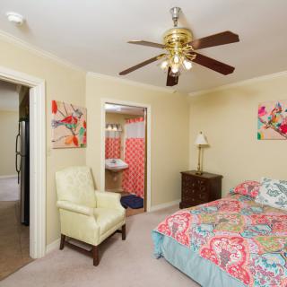 A cozy bedroom featuring a ceiling fan, colorful bedding, an armchair, and vibrant wall art.
