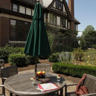 A cozy outdoor dining setup featuring a wooden table under a green umbrella, surrounded by lush gardens.