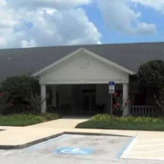 A building entrance with an accessible parking space in front, set against a cloudy sky.