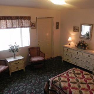 A cozy bedroom with a window, dresser, chairs, and a quilt-covered bed.