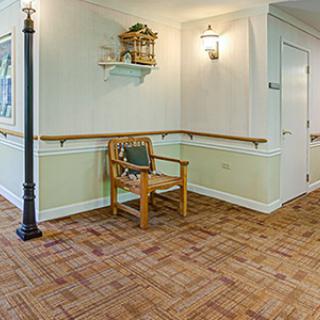 A cozy hallway with wooden flooring, featuring a chair, wall art, sconce lighting, and a floor lamp.