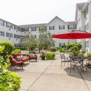A spacious courtyard with seating areas and a large red umbrella, surrounded by a multi-story apartment building.