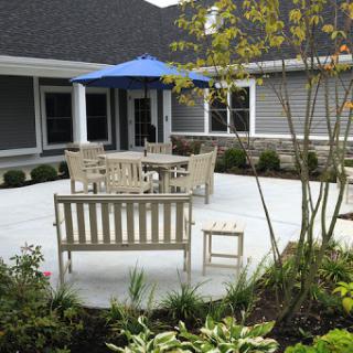 A serene outdoor patio setup featuring wooden furniture, an umbrella for shade, and lush greenery.