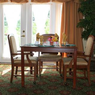 A well-lit dining area featuring a wooden table and four chairs, with large windows and curtains providing natural light.