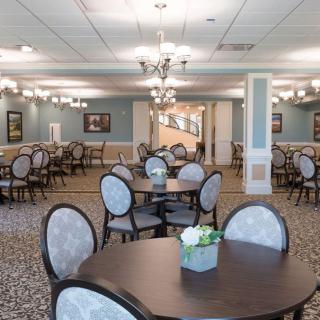 A spacious dining area with elegant decor, featuring multiple tables and chairs arranged neatly under stylish chandeliers.
