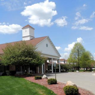 A picturesque building with a tower under a blue sky, surrounded by trees and landscaped grounds.
