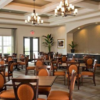An elegantly furnished dining room with wooden tables and orange-cushioned chairs under chandeliers.