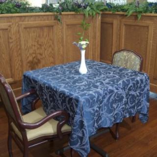 A dining table with a blue patterned tablecloth, accompanied by two chairs and a vase with flowers.