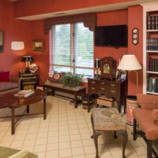 A cozy living room with traditional decor, featuring a sofa, coffee table, bookshelves, and a window with blinds.