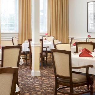 A neatly arranged dining room with tables set with white tablecloths and red napkins.