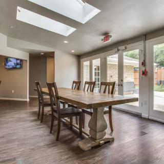 A modern dining room with a long wooden table, surrounded by chairs, featuring skylights and glass doors leading outside.