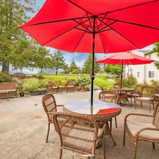 A peaceful patio with wicker chairs and tables under red umbrellas, overlooking a scenic garden.