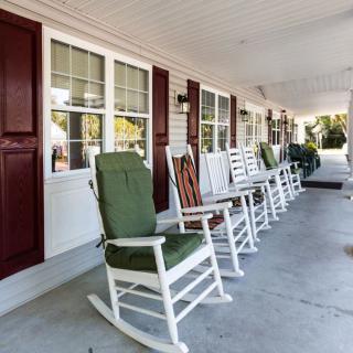 A row of rocking chairs with cushions lined up on a porch, offering a comfortable outdoor seating area.