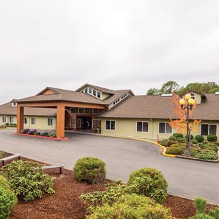 A hotel building with a well-maintained garden and a parking area at the front.