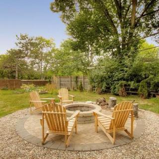 A cozy backyard setup featuring a fire pit surrounded by wooden chairs and lush greenery.
