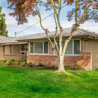 A suburban house with a brick facade, a well-maintained lawn, and a mature tree in the front yard.