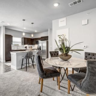 A modern open-concept kitchen and dining area featuring a marble dining table, bar stools at the island counter, and stainless steel appliances.