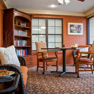 A cozy reading room with a bookshelf, table, and chairs.