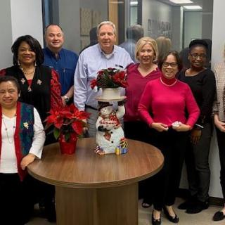 A group of people standing around a table with Christmas decorations in an office setting.