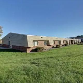 A row of single-story buildings with a grassy lawn under a clear blue sky.