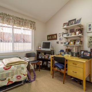 A cozy bedroom with a small workspace, featuring a desk and shelves filled with framed pictures.