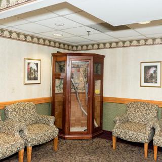 A cozy waiting area with patterned chairs and a decorative wooden cabinet, surrounded by framed artwork on the walls.