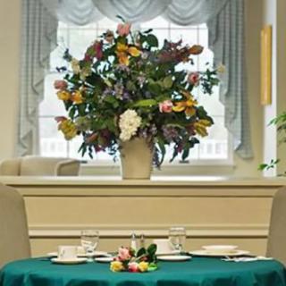 A beautifully arranged flower centerpiece on a dining table set against a window with elegant curtains.