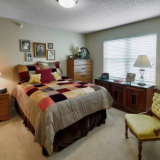 A cozy bedroom featuring a bed with colorful pillows, wooden furniture, and framed wall art.