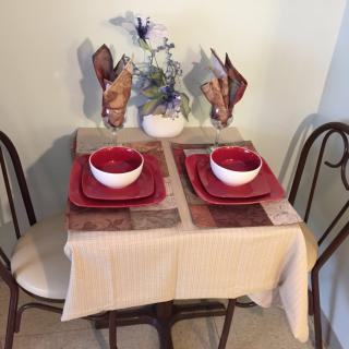 A cozy dining setup for two with red and white dinnerware on a small table, adorned with a floral centerpiece.