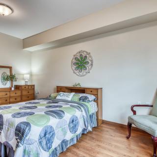 A cozy bedroom featuring a bed with a patterned quilt, wooden furniture, and a decorative wall piece.