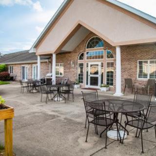 A patio area with metal tables and chairs in front of a brick building with arched windows.